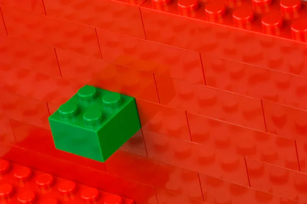 Green building block in a wall of red one — Stock Photo, Image