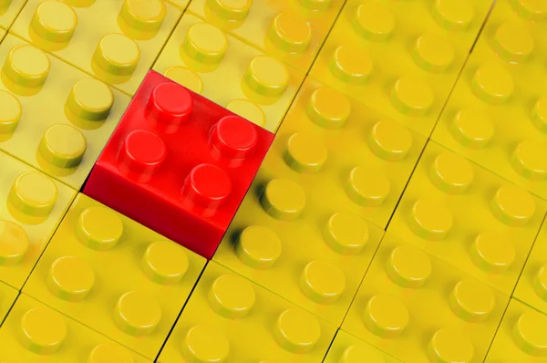 Red building block in a field of yellow ones — Stock Photo, Image