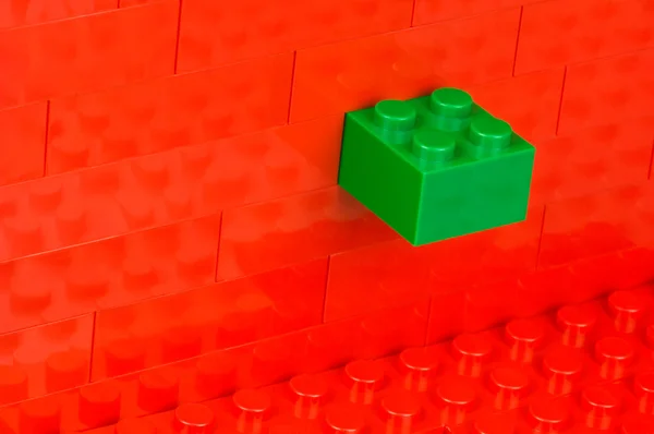 Green building block in a wall of red ones — Stock Photo, Image