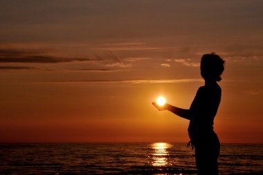 Woman silhouette at sunset as like holding the sun clipart