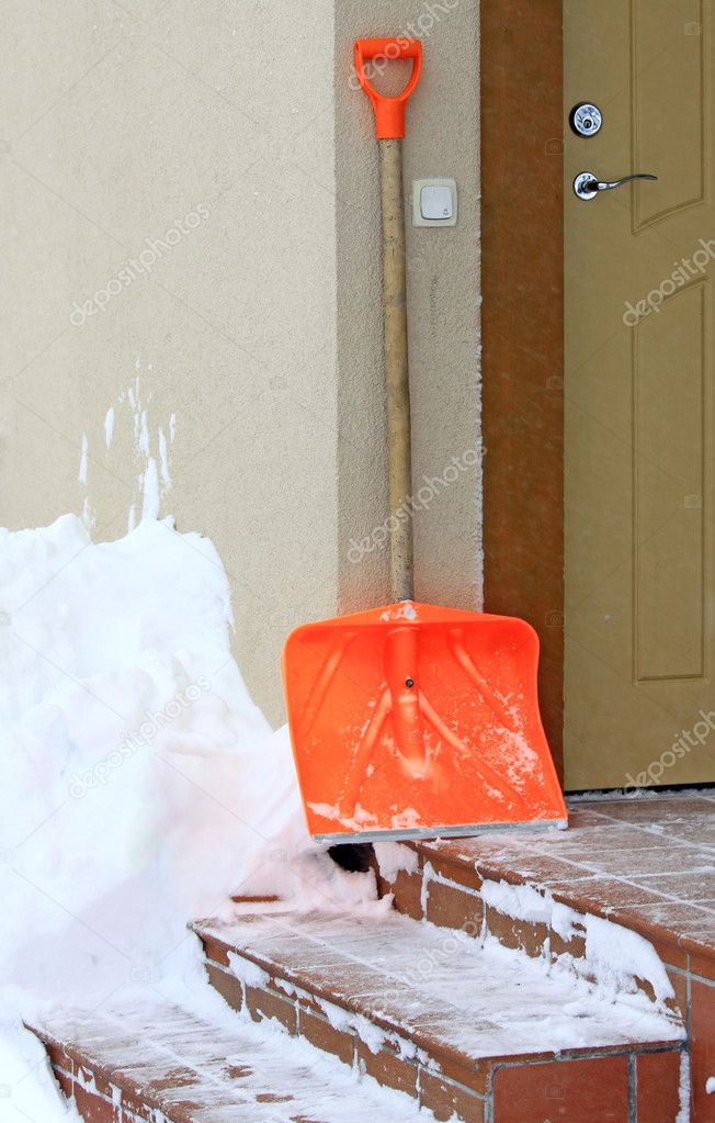 Snow shovel standing on the steps beside front door