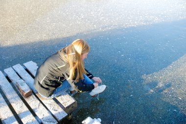 Young woman going to skate on frozen lake putting her ice skating shoes on. clipart