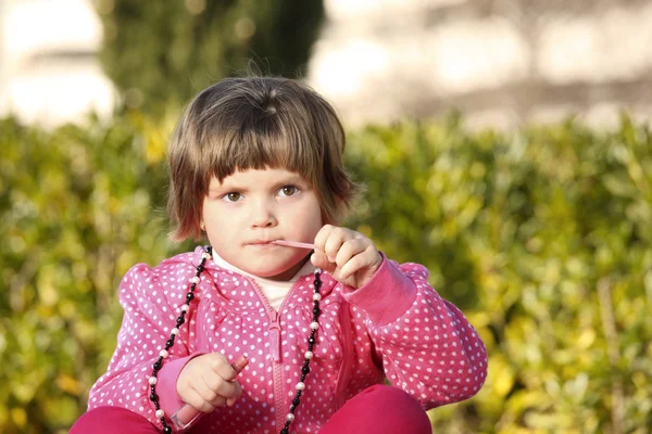 一个小女孩坐在公园和试图使用唇彩的图片 — 图库照片