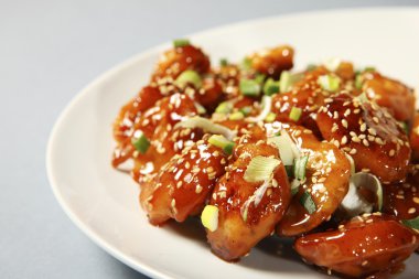 A close-up of a portion of sesame chicken served on a white plate clipart