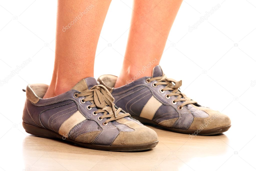 A closeup of female legs trying on too big male shoes over white background