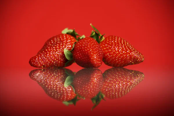 Tre jordgubbar mot röd bakgrund — Stockfoto