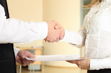 Man and woman shaking hands in office and giving papers clipart