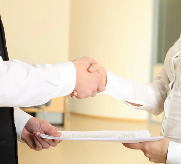 Man en vrouw schudden handen in office en geven papieren — Stockfoto