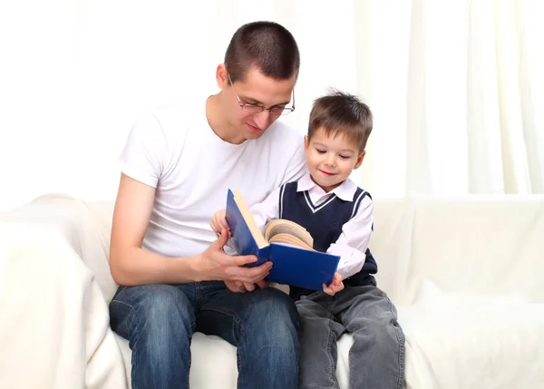 Far och son läser en bok på soffa — Stockfoto