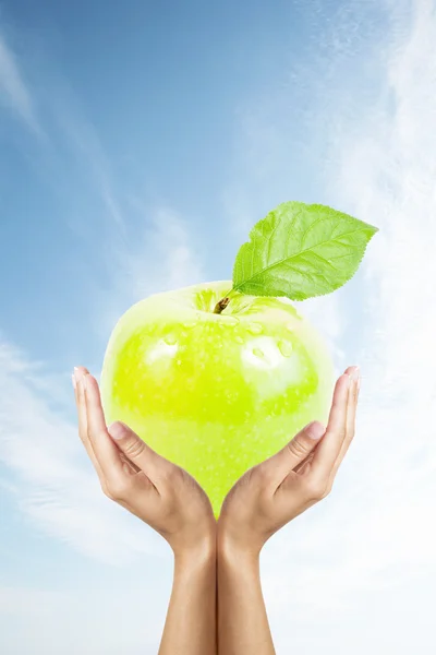 Green apple in hands over sky — Stock Photo, Image