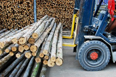 Truck loading pile of wood in logs storage for construction or industrial work clipart