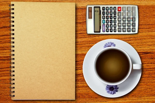 白杯咖啡和木桌背景上的笔记本上的计算器 — 图库照片