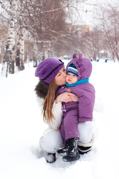 Matka całuje i przytrzymanie dziecka, śnieg, zima park, spacer — Zdjęcie stockowe