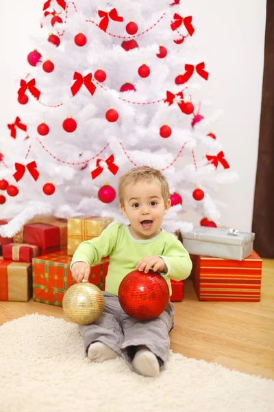 Niño Feliz Sentado Frente Árbol Navidad Sosteniendo Grandes Adornos Rojos —  Fotos de Stock