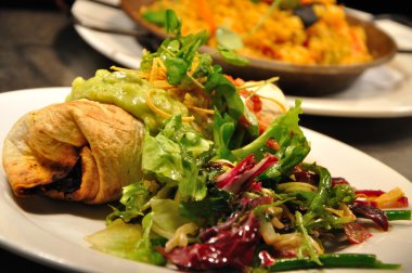 Beef burrito with salad, guacamole, salsa and paella in the background clipart