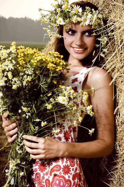 Schöne Frau mit Blumen in der Nähe eines Heuhaufens — Stockfoto