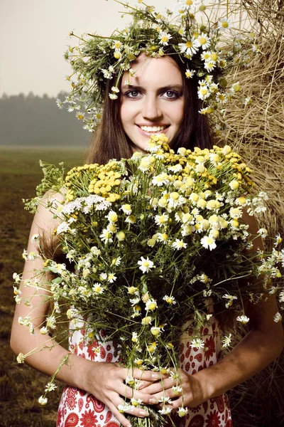 Belle femme avec des fleurs près d'une botte de foin — Photo