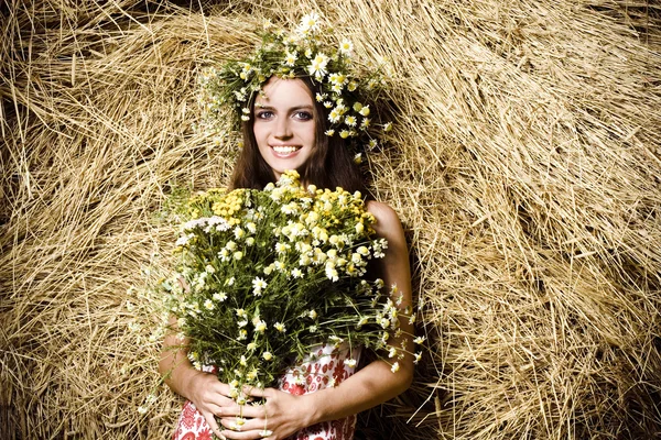 Όμορφη γυναίκα με λουλούδια, κοντά σε μια θυμωνιά χόρτου — Φωτογραφία Αρχείου