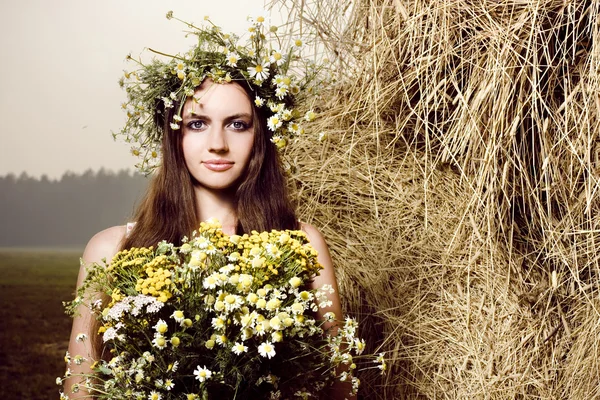 Όμορφη γυναίκα με λουλούδια, κοντά σε μια θυμωνιά χόρτου — Φωτογραφία Αρχείου