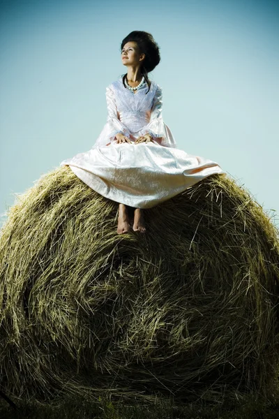 ヴィンテージのドレスを干し草の山の上に座ってで美しい女性 — ストック写真
