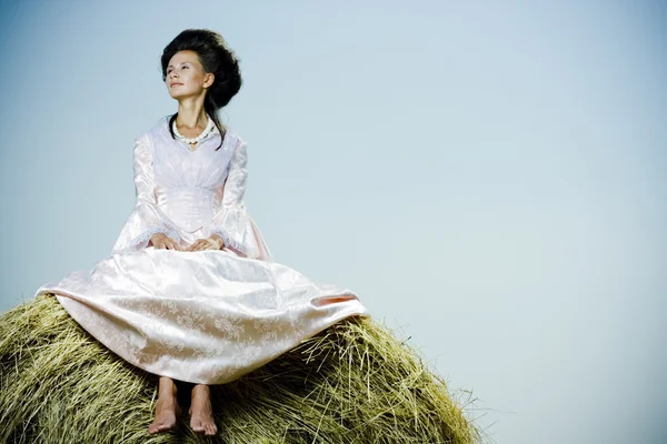 Красива жінка в вінтажній сукні, що сидить на стовбурі сіна — стокове фото