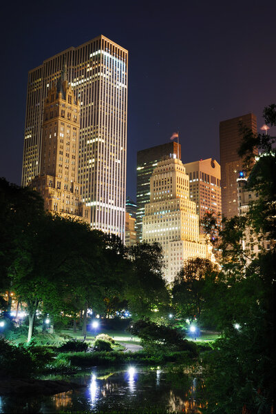 New York City Central Park at night with Manhattan skyscrapers lit with light.