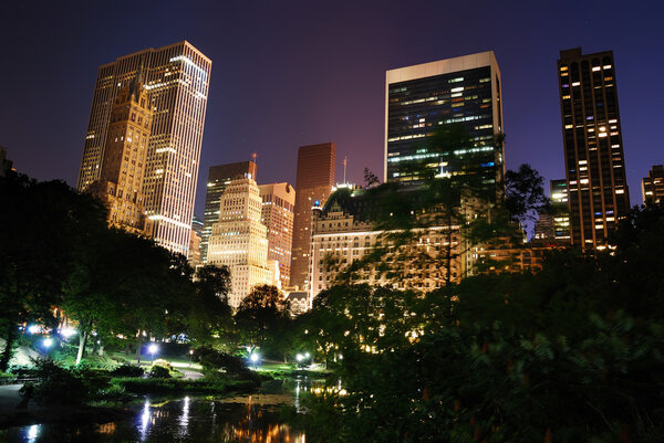 New York City Central Park at night with Manhattan skyscrapers lit with light.