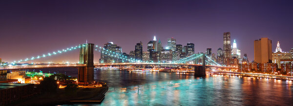 New York City Brooklyn Bridge and Manhattan skyline panorama view with skyscrapers over Hudson River illuminated with lights at dusk after sunset.