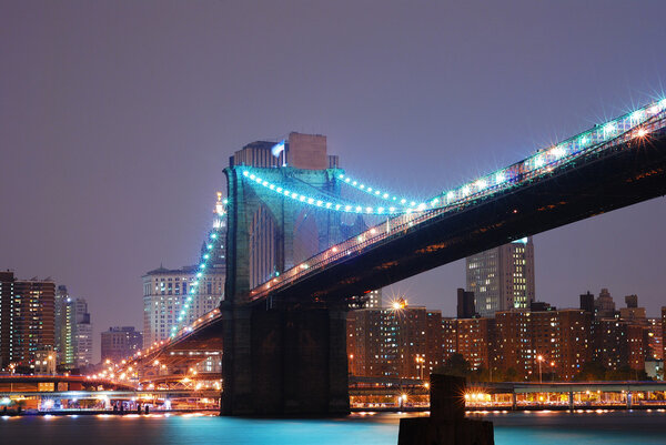 Brooklyn bridge at night with New York City skyline over Hudson River.