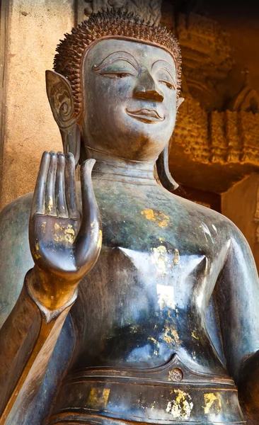 青铜佛图像中站立姿势与手工制作的砂岩教堂前举起右手 — 图库照片