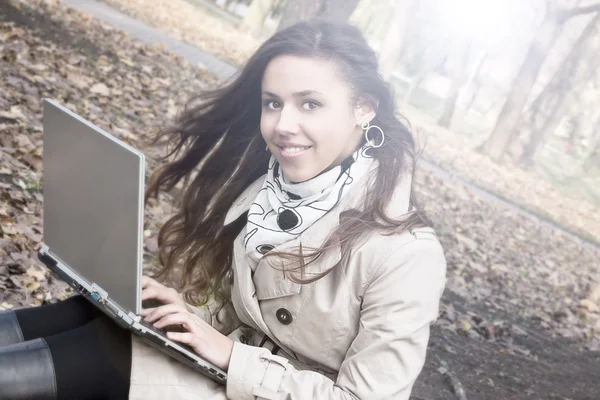 微笑着用一台笔记本电脑在公园里的年轻黑发女孩 — 图库照片