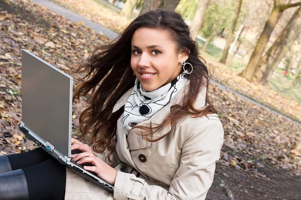 Vacker ung flicka som håller en laptop i en park — Stockfoto