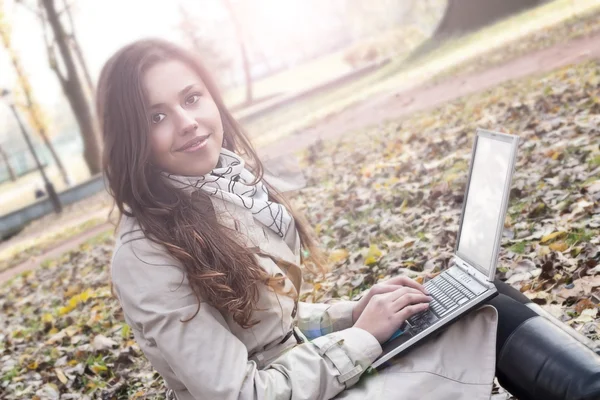 Lachende brunette meisje met een laptop werkt — Stockfoto