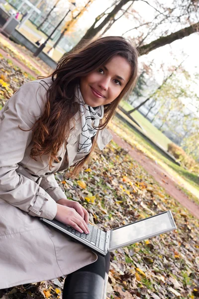 Charmiga brunett tjej med en laptop i parken — Stockfoto