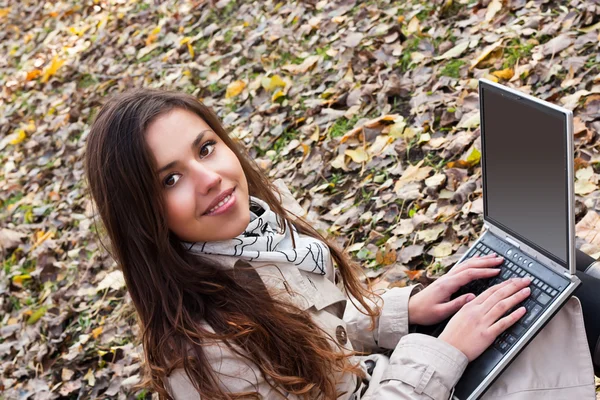 用一台笔记本电脑在公园里的漂亮黑发女孩 — 图库照片