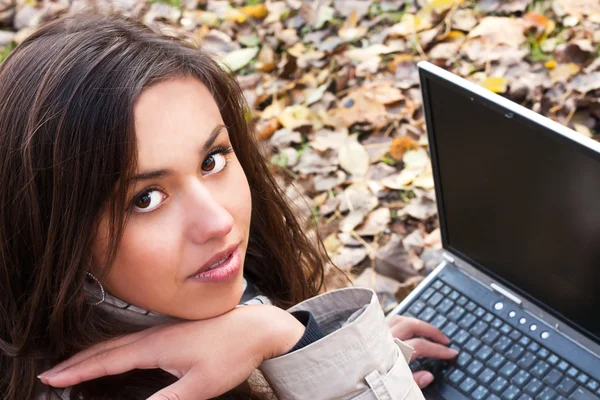 Charmante brunette meisje met een laptop in het park — Stockfoto
