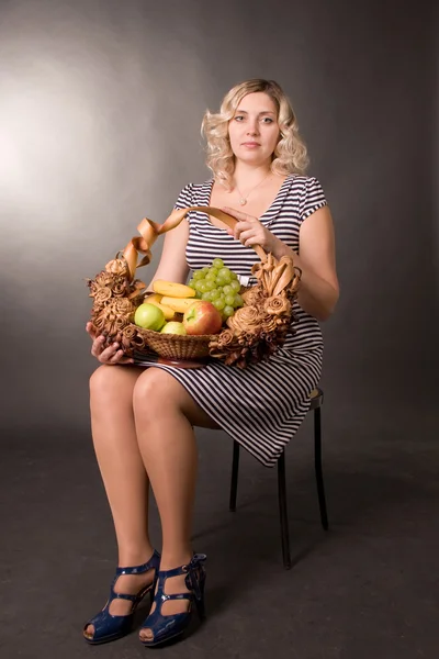 Hermosa joven se sienta en una silla y sostiene una cesta con fruta —  Fotos de Stock
