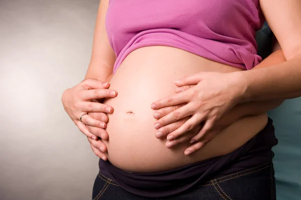 Foto de la mujer embarazada y su marido está en un estudio. Abraza las manos del estómago —  Fotos de Stock