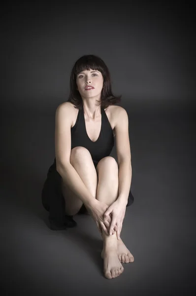 スタジオの床に座って 暗い背景に若い魅力的な若い女性の肖像画 — ストック写真