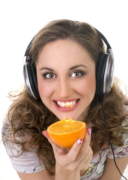 Meisje muziek luistert en eet oranje — Stockfoto