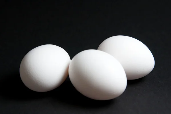 Три белых яйца на черном фоне — стоковое фото