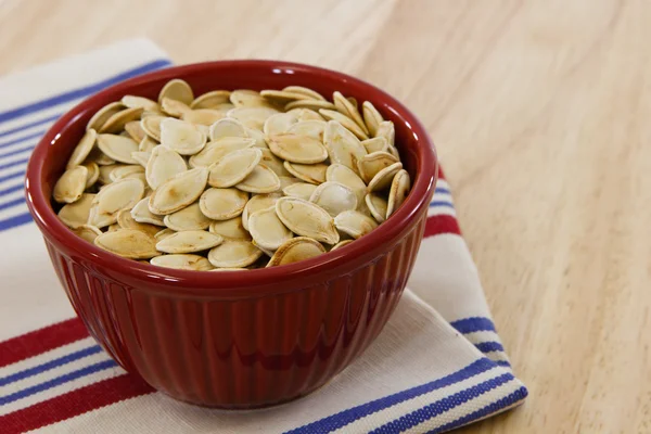 Red bowl brimming with toasted pumpkin seeds — Stock Photo, Image