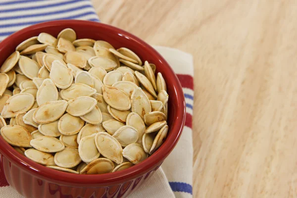Toasted pumpkin seeds in a red bowl with copy space — Stock Photo, Image
