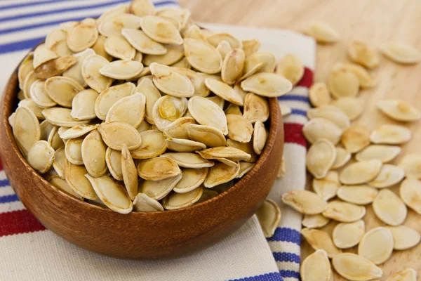 Toasted pumpkin seeds overflowing a wooden bowl — Stock Photo, Image
