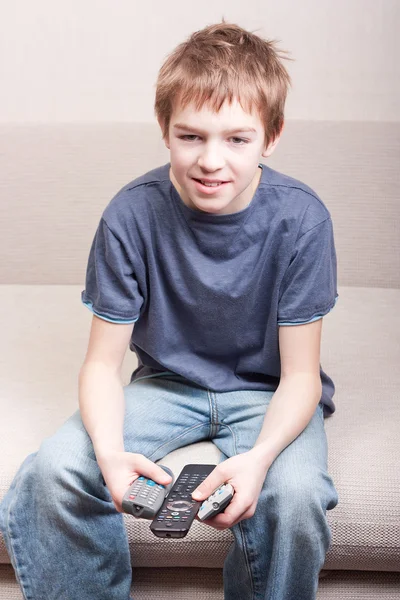 Teen watches television and holds three remote — ストック写真