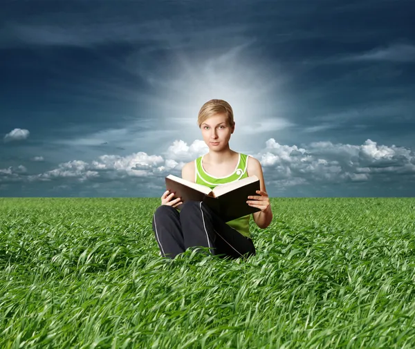 College girl lettura grande libro in erba verde — Foto Stock