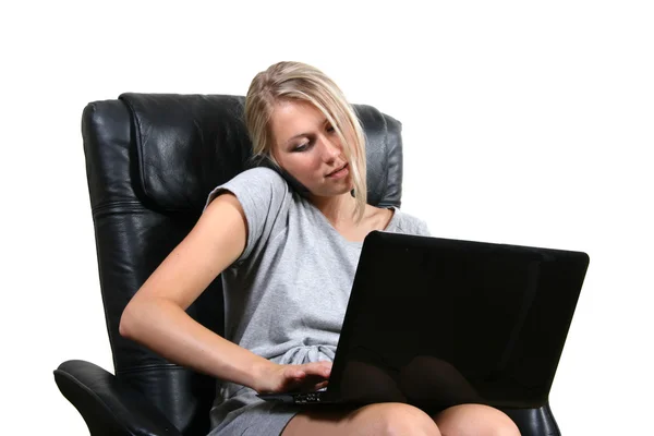 Жінка сидить у кріслі з ноутбуком і розмовляє по телефону — стокове фото