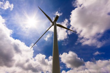 Wind turbine over a cloud filled blue sky, alternative energy so clipart