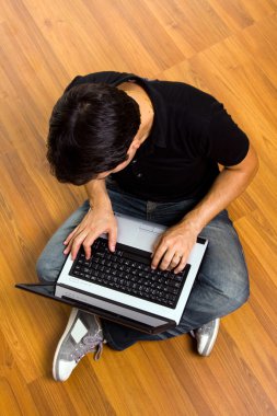 Young man sitting on the floor working on laptop computer at hom clipart