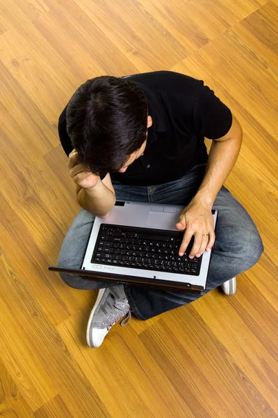 紅のラップトップ コンピューターで作業して床に座っている若い男 — ストック写真